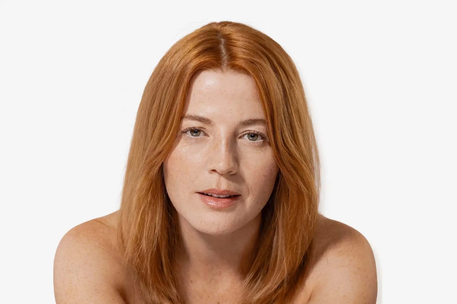 A close-up portrait of a woman with shoulder-length red hair and a subtle smile, showcasing her skincare routine results, posing against a white background