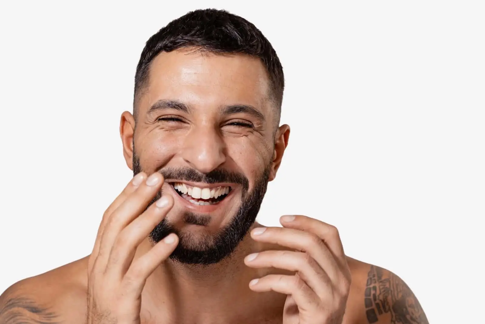 Ein fröhlicher Mann mit strahlender Haut, der lacht, während er sein Gesicht berührt, isoliert auf einem weißen Hintergrund