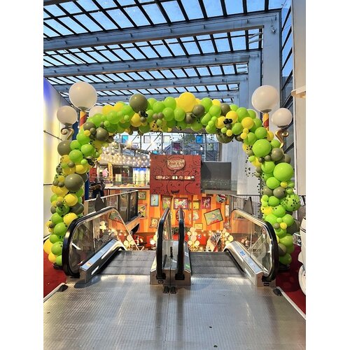 Grote groen-gele ballonnenboog boven de roltrappen bij Plopsa Station