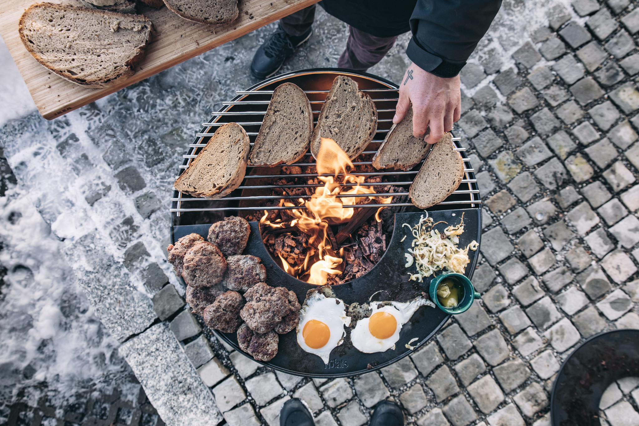 Man met tattoo roostert eten op een openvuur grill van Höfats