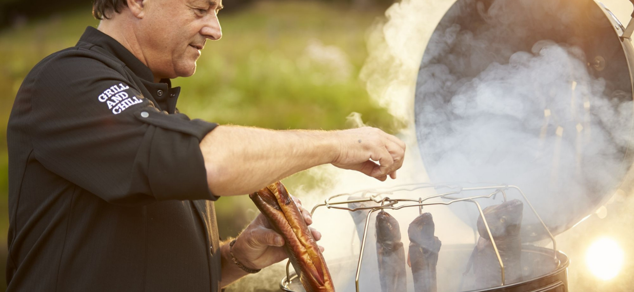 Man van middelbare leeftijd rookt vis in een Rösle barbecuetoestel