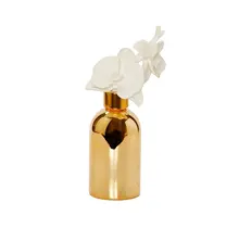 Diffuseur de bouteille en or Vivience avec capuchon doré et fleur blanche, parfum « Muguet »