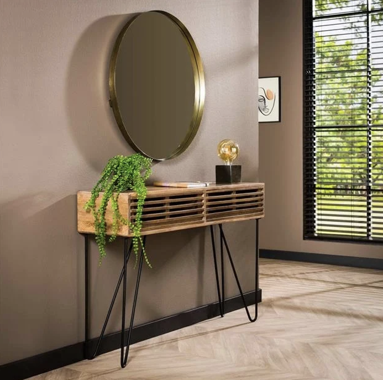 Houten kaptafel met metalen poten, ronde spiegel en groene plant in een warme zandkleurige setting.