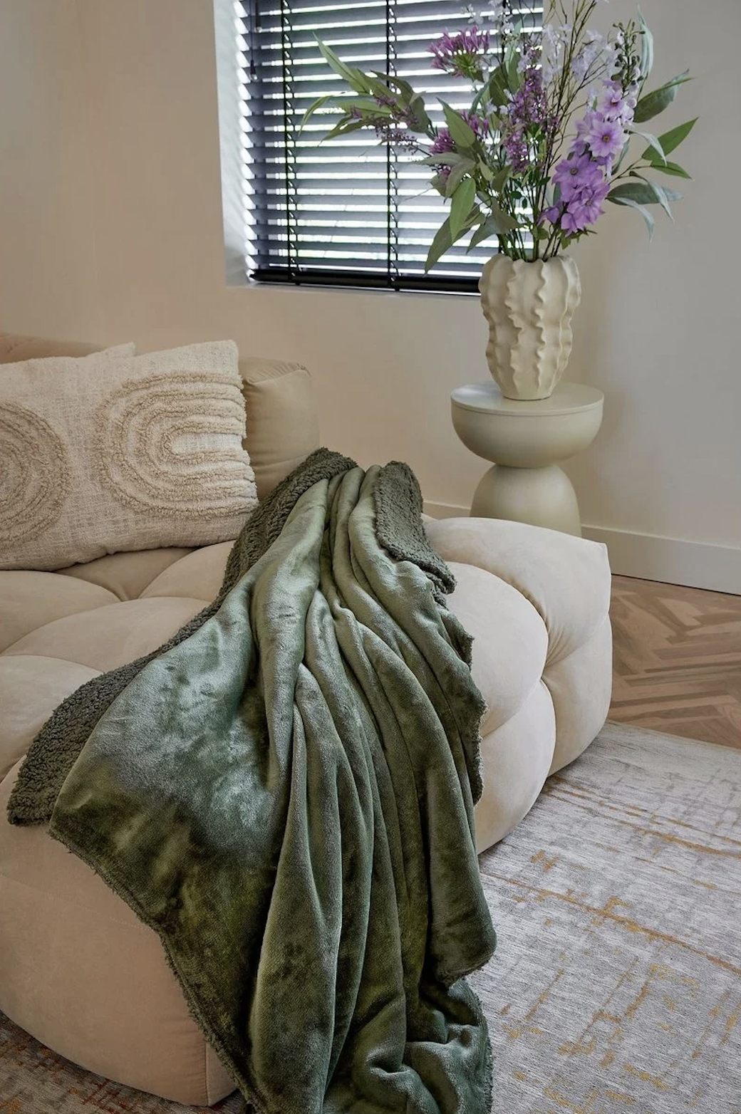 Donkergroene fleece plaid op zachte bank met bloemen – natuurlijke materialen en rust in huis.