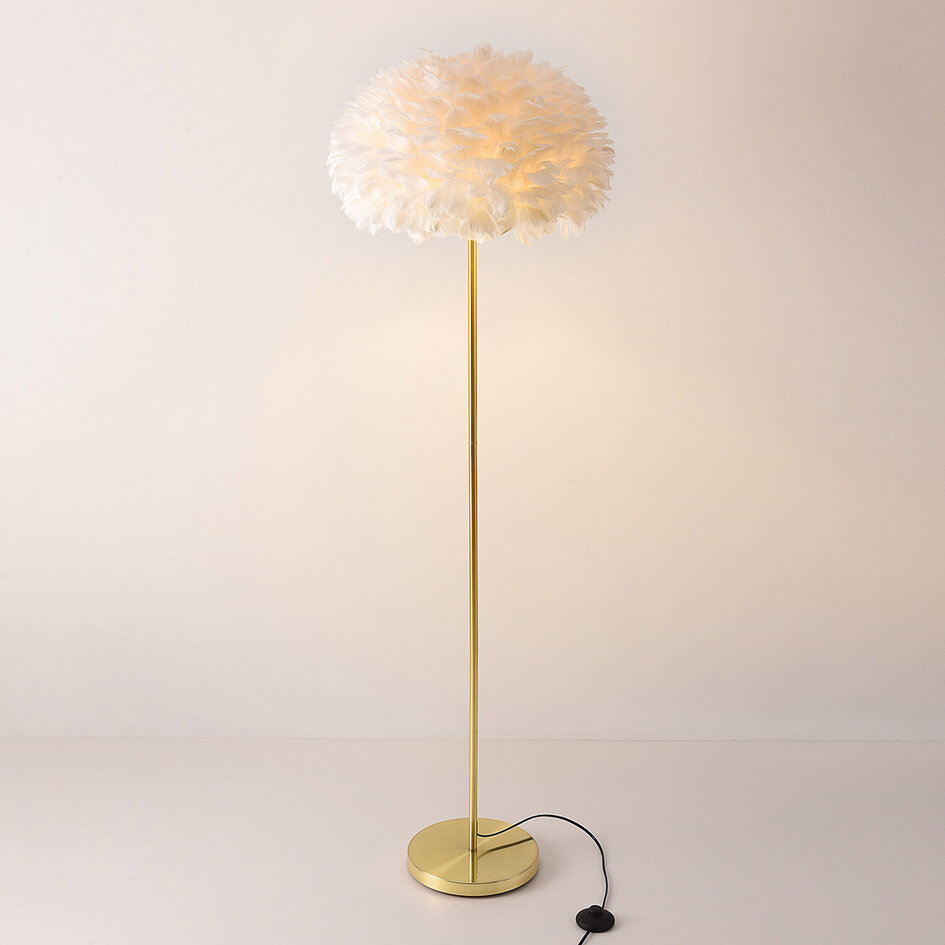 Designad golvlampa Evania med vita fjädrar och fot i guldmässing