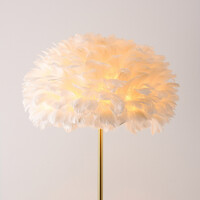 Designad golvlampa Evania med vita fjädrar och fot i guldmässing