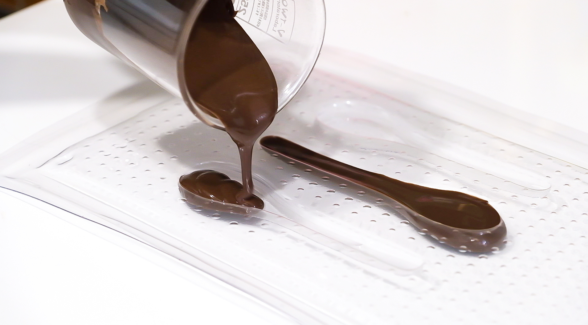 Chocolate being poured in a custom vacuum formed chocolate mould in the shape of a spoon