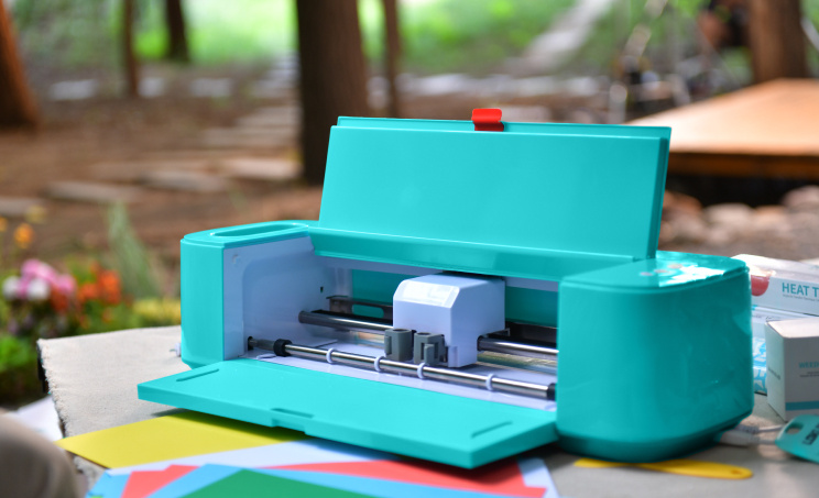 LOKLiK Crafter LOKLiK Blue open on a table in nature with on the table in front of the machine some card stock papers ready to cut.
