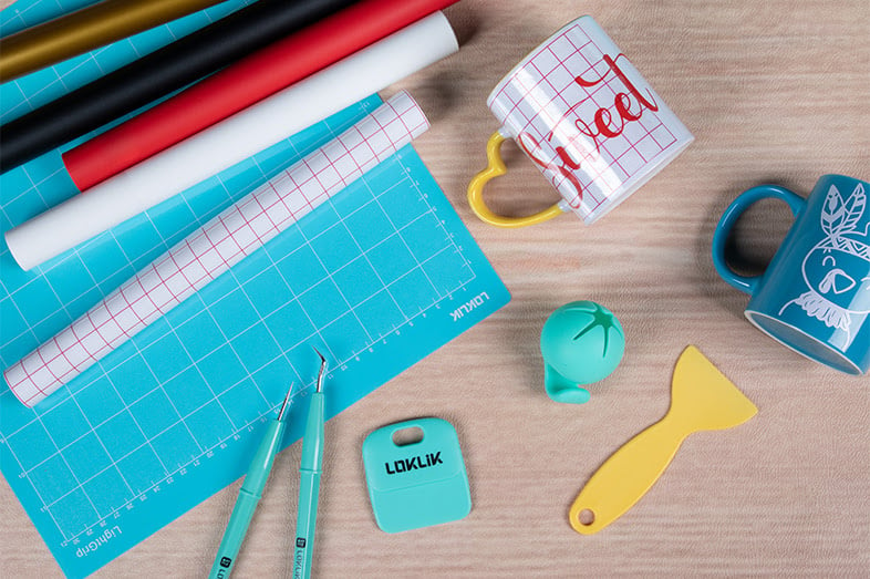 Top view of contents of the LOKLiK Starter Bundle showing LOKLiK weeding tools, blue cutting mat, Heat Transfer Vinyl rolls, grid tape and some example mugs.