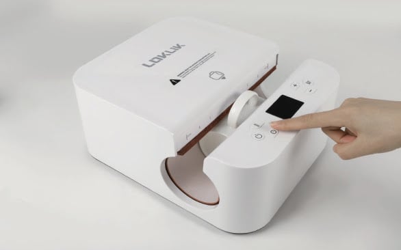 LOKLiK Auto Tumbler Heat Press seen at an angle with a mug inserted into it. A hand is reaching out and pressing the timer button.