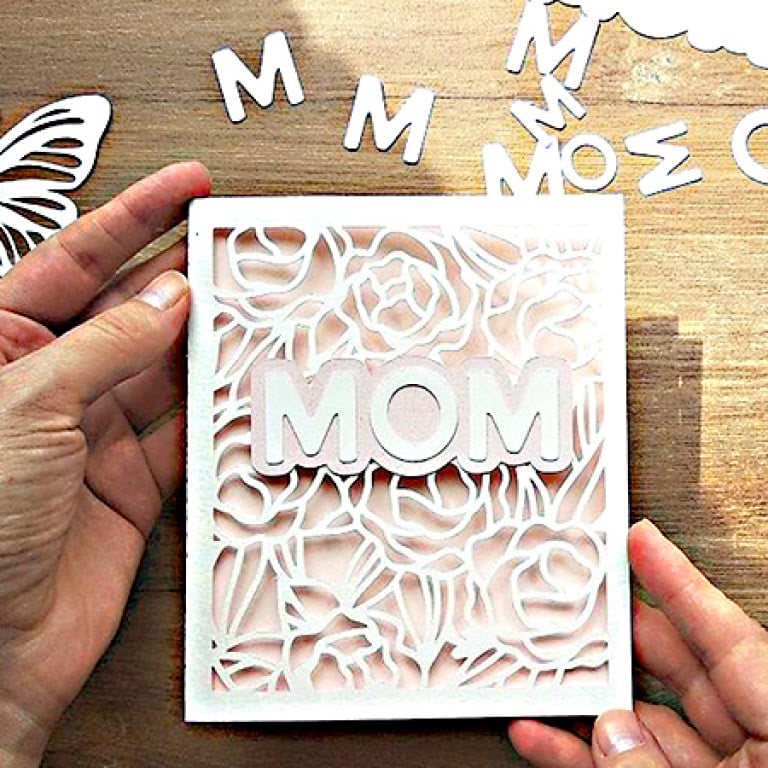 Hands holding an intricately cut card with the word 'mom' in the center.