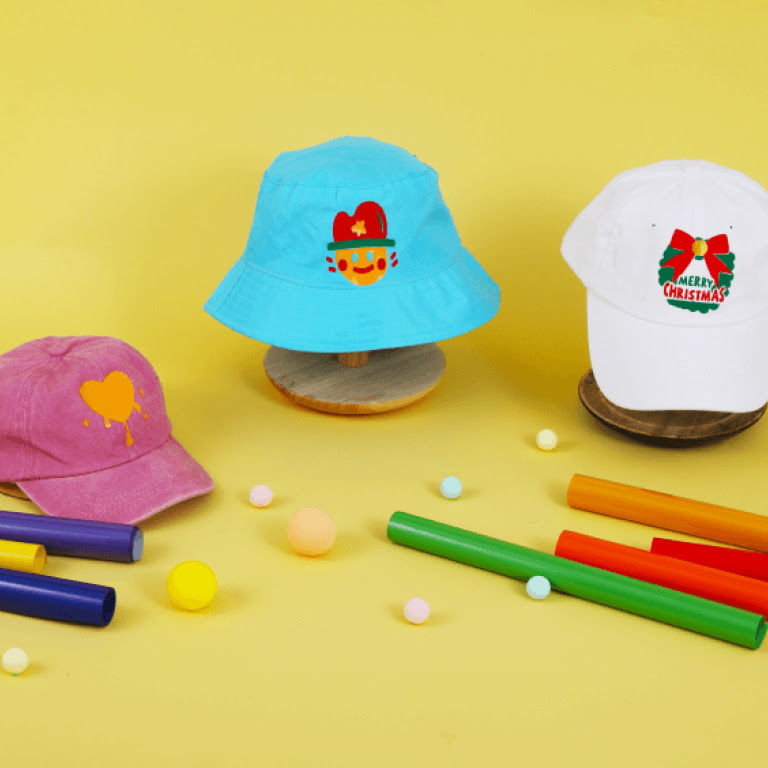 Pink cap with an orange vinyl iron on design, blue bucket hat with a cute figure in a hat and a white cap with a Christmas wreath.