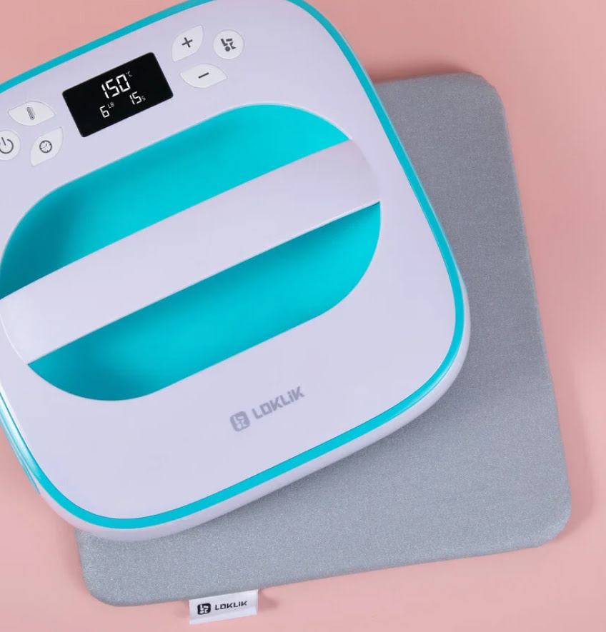 Top down view of a heat press mat and LOKLiK Easy Heat Press in LOKLiK Blue on a light pink table.