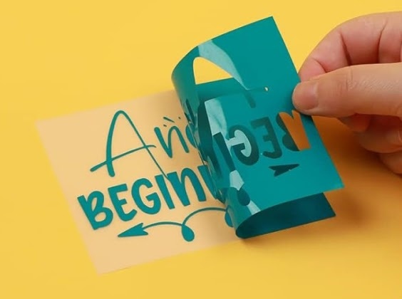 Hand peeling off excess teal permanent adhesive vinyl from the PET backing.