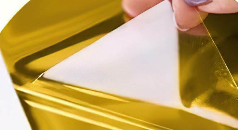 Estrazione a gancio della pellicola protettiva da un foglio di vinile adesivo permanente metallizzato a specchio oro.