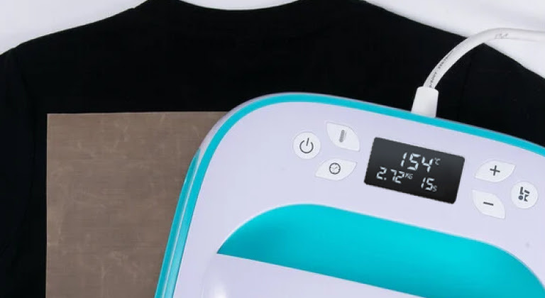 Close-up van een LOKLiK Easy Heat Press in LOKLiK Blue bovenop eenTeflon vel en een zwart T-shirt.