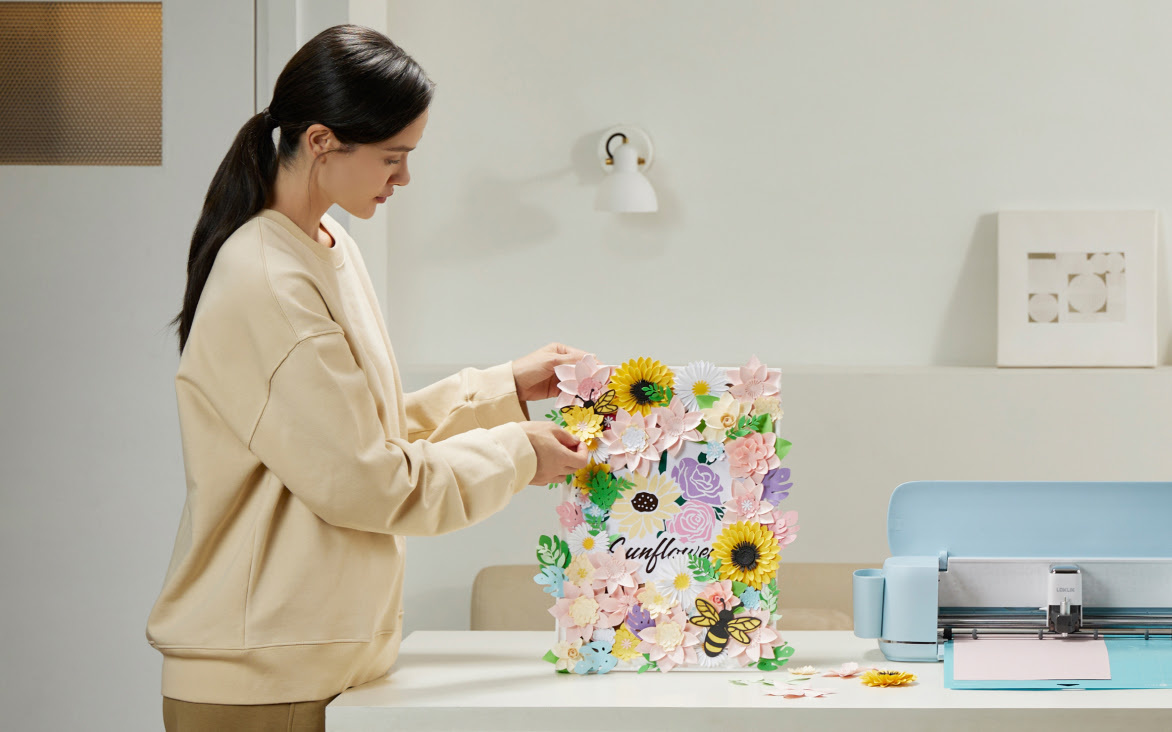 Woman fixing papercut flowers to a frame. On the table is a LOKLiK iCraft in bubble blue™