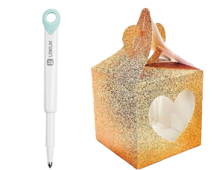 Scoring-Stift für den LOKLiK iCraft™. Rechts ist eine Faltschachtel aus orangefarbenem Glitzerkarton. Auf einer Seite ist ein Herz ausgeschnitten.