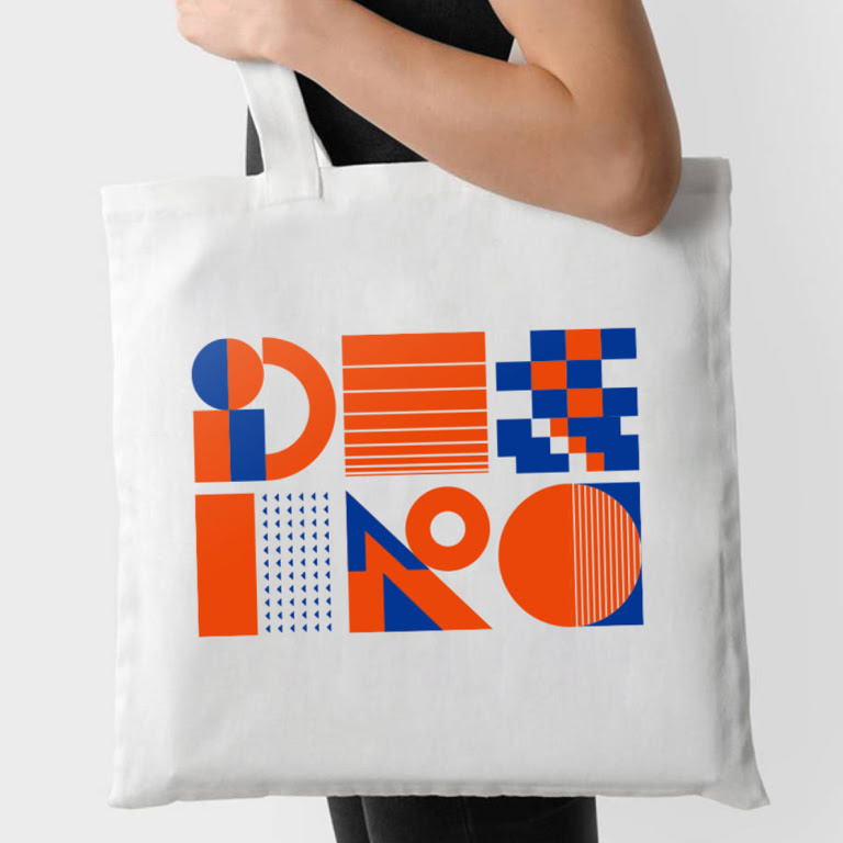 Person holding a white tote bag with a heat transfer design of abstract shapes in blue and orange heat transfer vinyl.