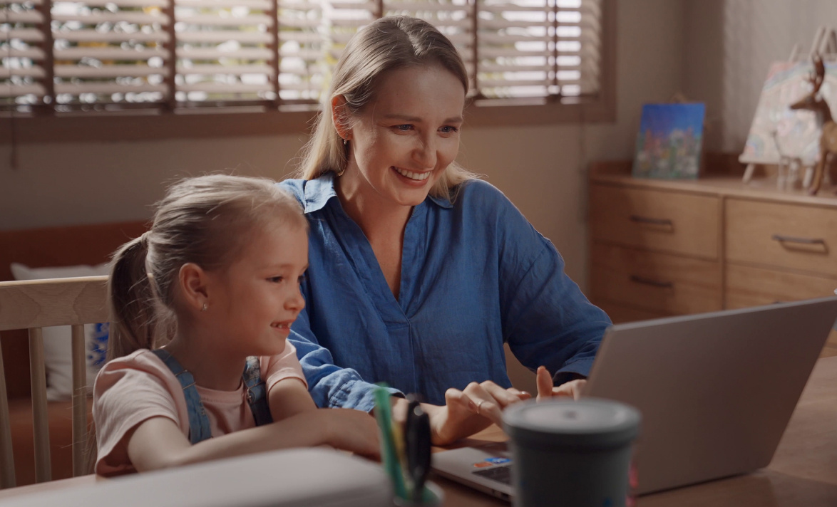 Woman and child sitting at a laptop on a desk. They smile and look at the screen.