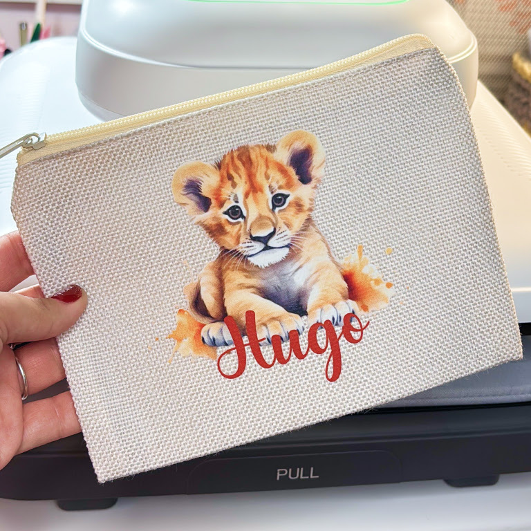 Hand holding a canvas pouch with a transfer print of a lion cub and the name Hugo.