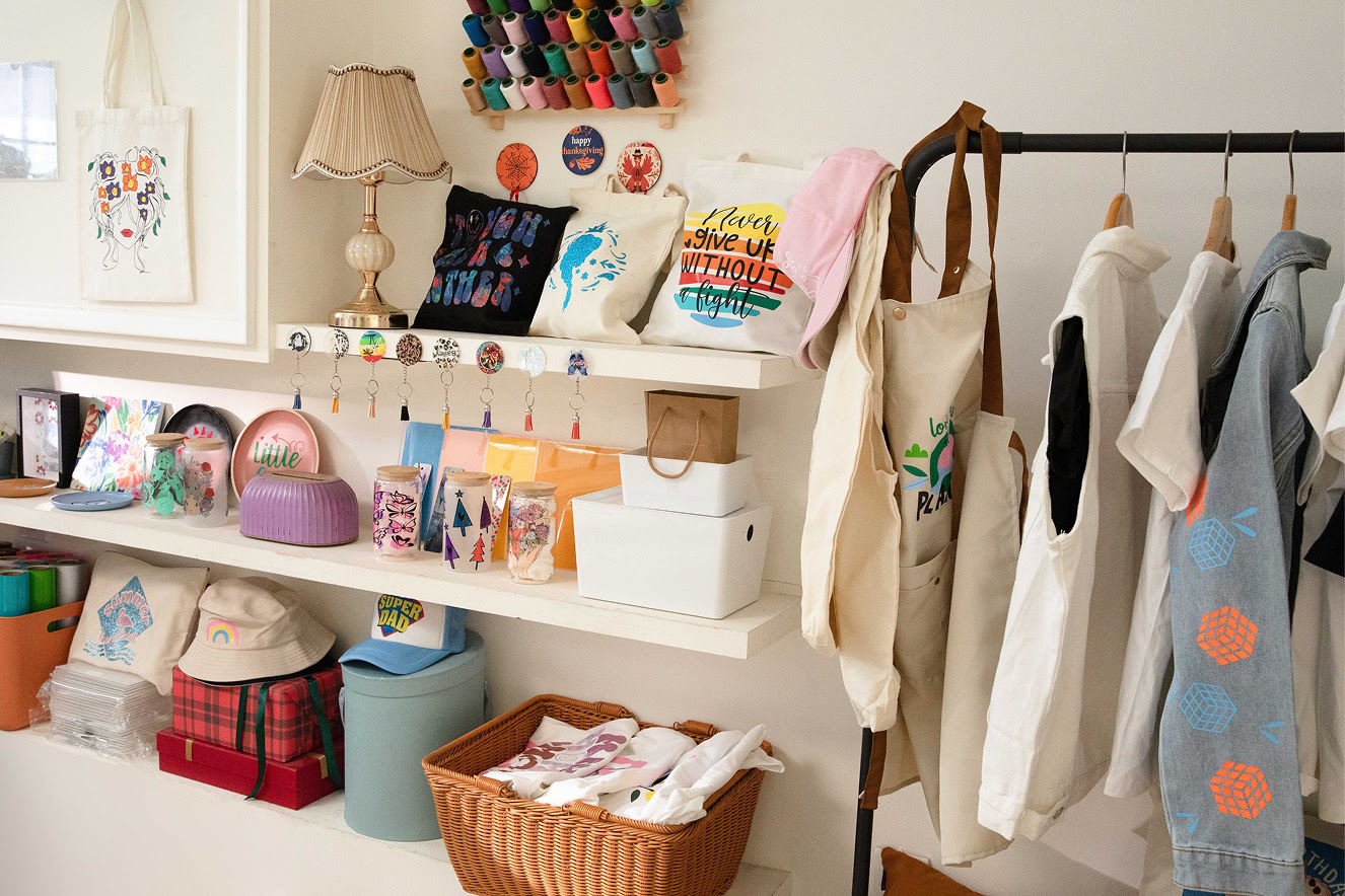 View of a shop interior showing shelves with custom products with heat transfer designs and a rack of clothing.