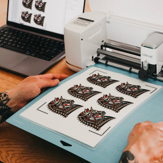 Two hands feeding taking a cutting mat out of a LOKLiK iCraft.  On the mat there are 6 illustrations of a gothic horse head.