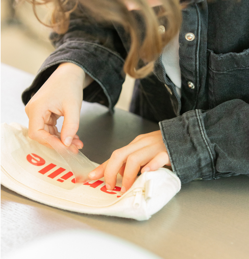 Enfant décollant le support d'un dessin transféré à chaud sur un étui à crayons.