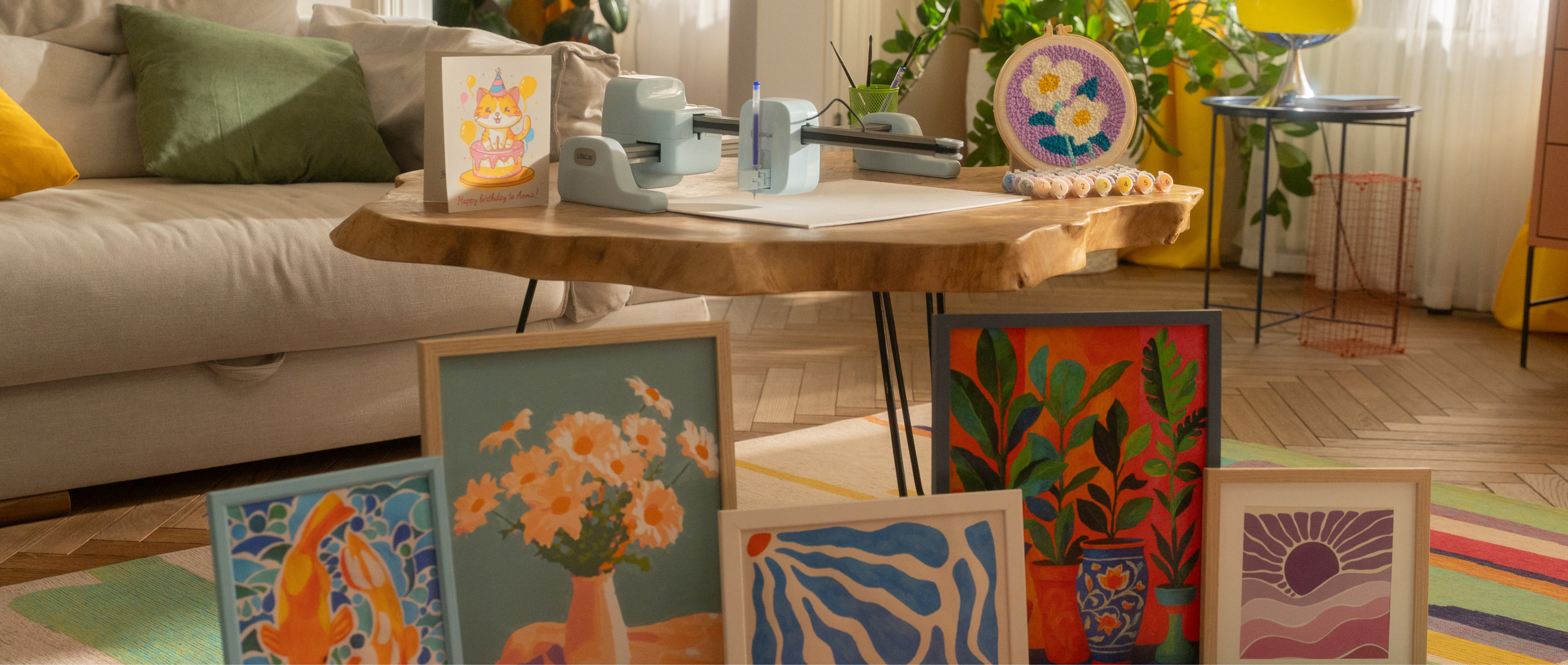 Huiselijke setting van een LOKLiK iPaint™ in Bubble Blue op een houten salontafel. Op de tafel staan ook kleine genummerde potjes verf netjes geordend, een borduurring met een getuft motief van twee witte bloemen tegen een paarse achtergrond en een verjaardagskaart met een kat. Verschillende andere voltooide verf-door-nummers kunstwerken staan tegen de salontafel geleund.