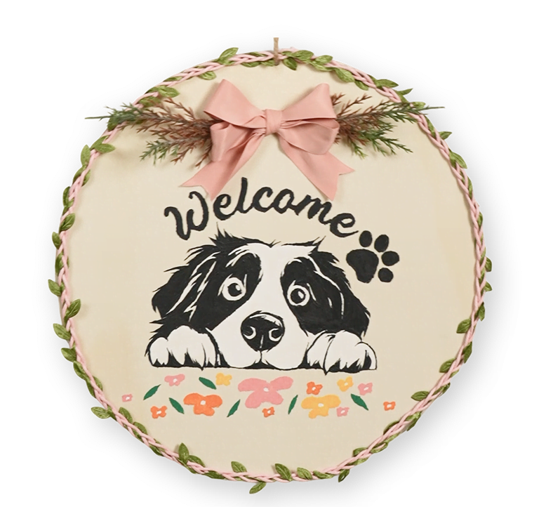 Disco in legno con un cane dipinto con i numeri, il testo Welcome e alcuni fiori. Il disco di legno è decorato con un nastro.