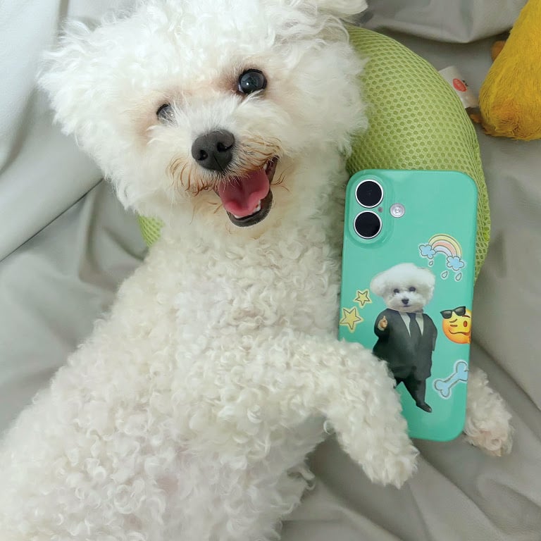 Cute little white dog lying down with a heat pressed phone case between its paws. The phone case has a similar white dog in a suit.