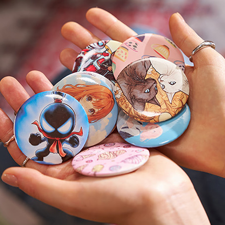 Two hands holding a set of heat pressed button pins.