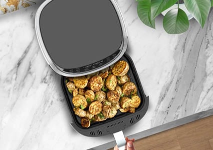 Een zwarte airfryer die gevuld is met gebakken aardappels