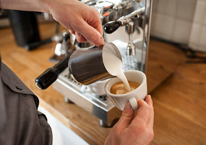 Iemand die melk inschenkt in een kop koffie