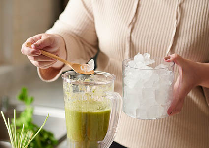 Een vrouw die ijs toevoegt aan de smoothie in de blender