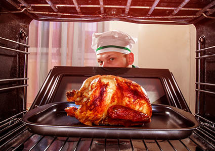 Een meneer die de oven open doet en kijkt of de kip goed gebraden is
