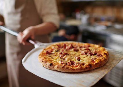 Een persoon die een versgebakken pizza uit de oven haalt