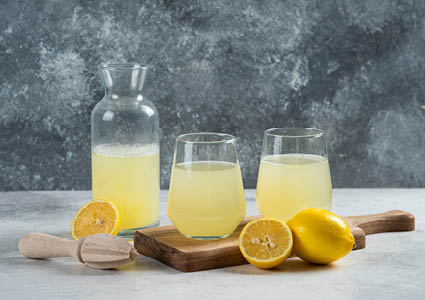 Een houten snijplank met daarop drinkglazen en een karaf gevuld met limonade