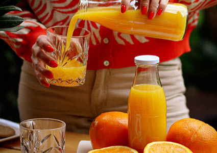 Een vrouw die sinaasappelsap aan het inschenken is in een drinkglas