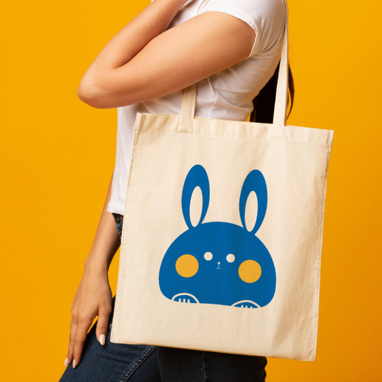 Side view of a woman having a white tote bag with a cute blue rabbit over her shoulder. 