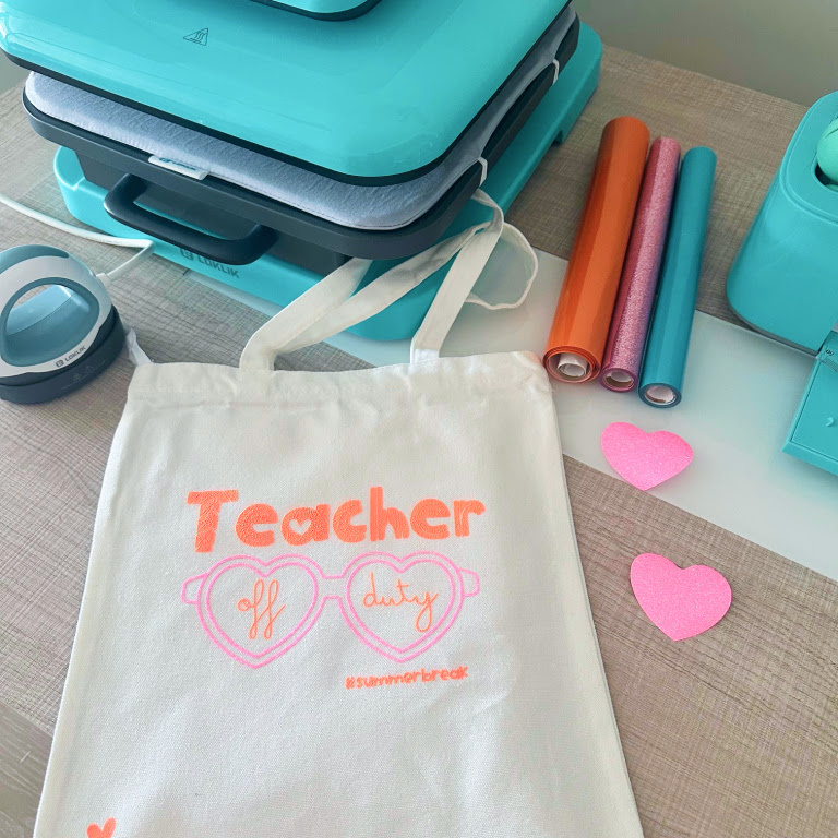 White tote back with a heat transfer design in pink and orange with the text Teacher and heart-shaped sunglasses that have the words off duty on them.