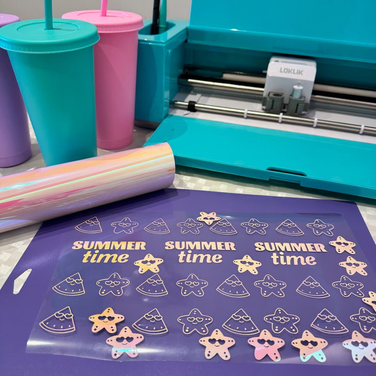 Purple LOKLiK Cutting mat with cute stars and pieces of watermelon cut out of holographic vinyl. In the back there is a LOKLiK Crafter and three cups with a straw.