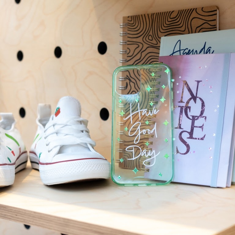 White canvas shoes with small cacti in heat transfer vinyl ironed on. A clear plastic phone cas with the text 'Have good day' and a notebook with 'notes' in permanent vinyl.