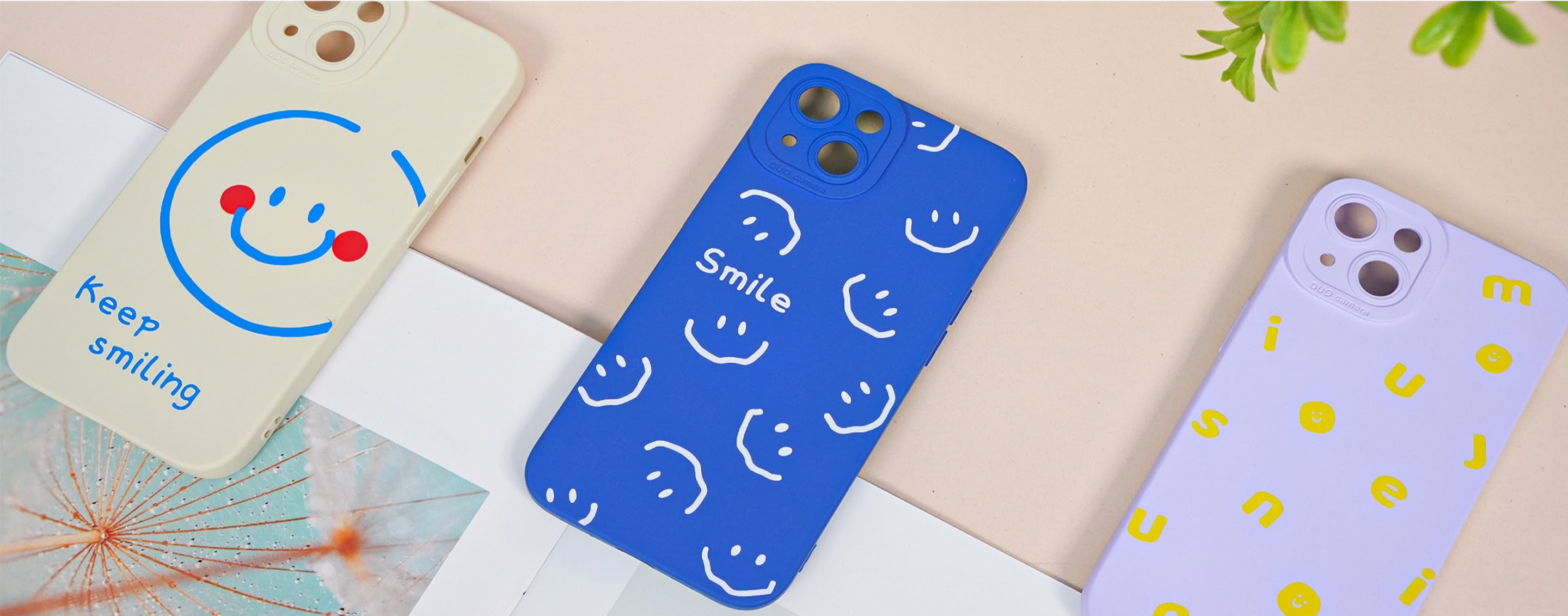 Three phone cases next to each other. The first has a permanent vinyl decal with a smiley and the words 'Keep smiling'. The second blue phone case has a permanent vinyl pattern of white smileys and the word 'smile'. The last phone case is lilac and has a pattern of different yellow letters and smileys in permanent adhesive vinyl.