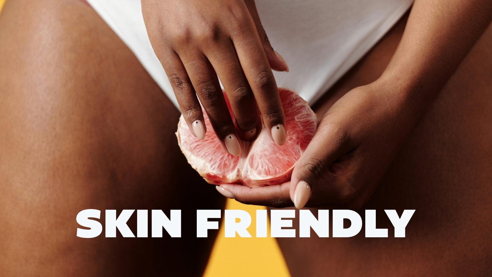 Close-up of hands holding and touching a halved grapefruit, symbolizing intimacy, with the text "Skin Friendly"