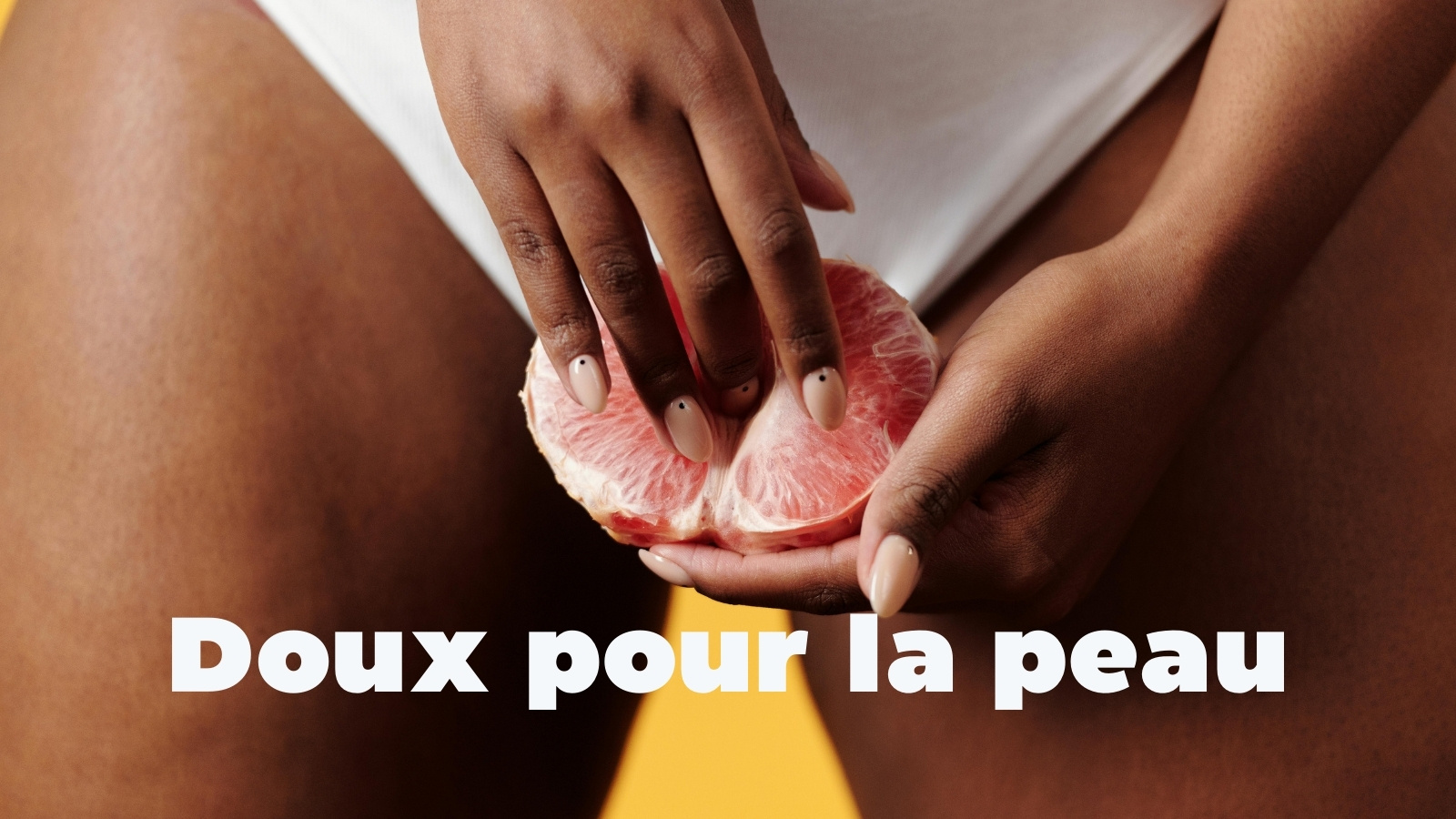 Gros plan de mains tenant et caressant un pamplemousse coupé en deux, symbole d’intimité, avec le texte "Respectueux de la peau"