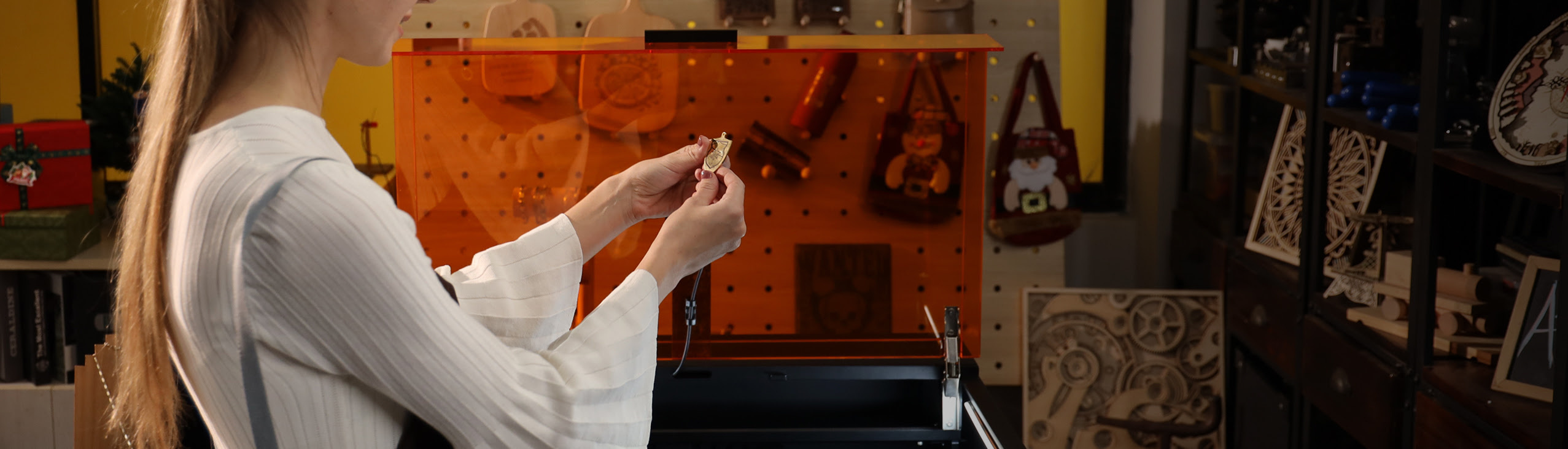 Woman in a workshop holding a piece of engraved metal. In the background is an AtomStack Kraft with the lid opened.