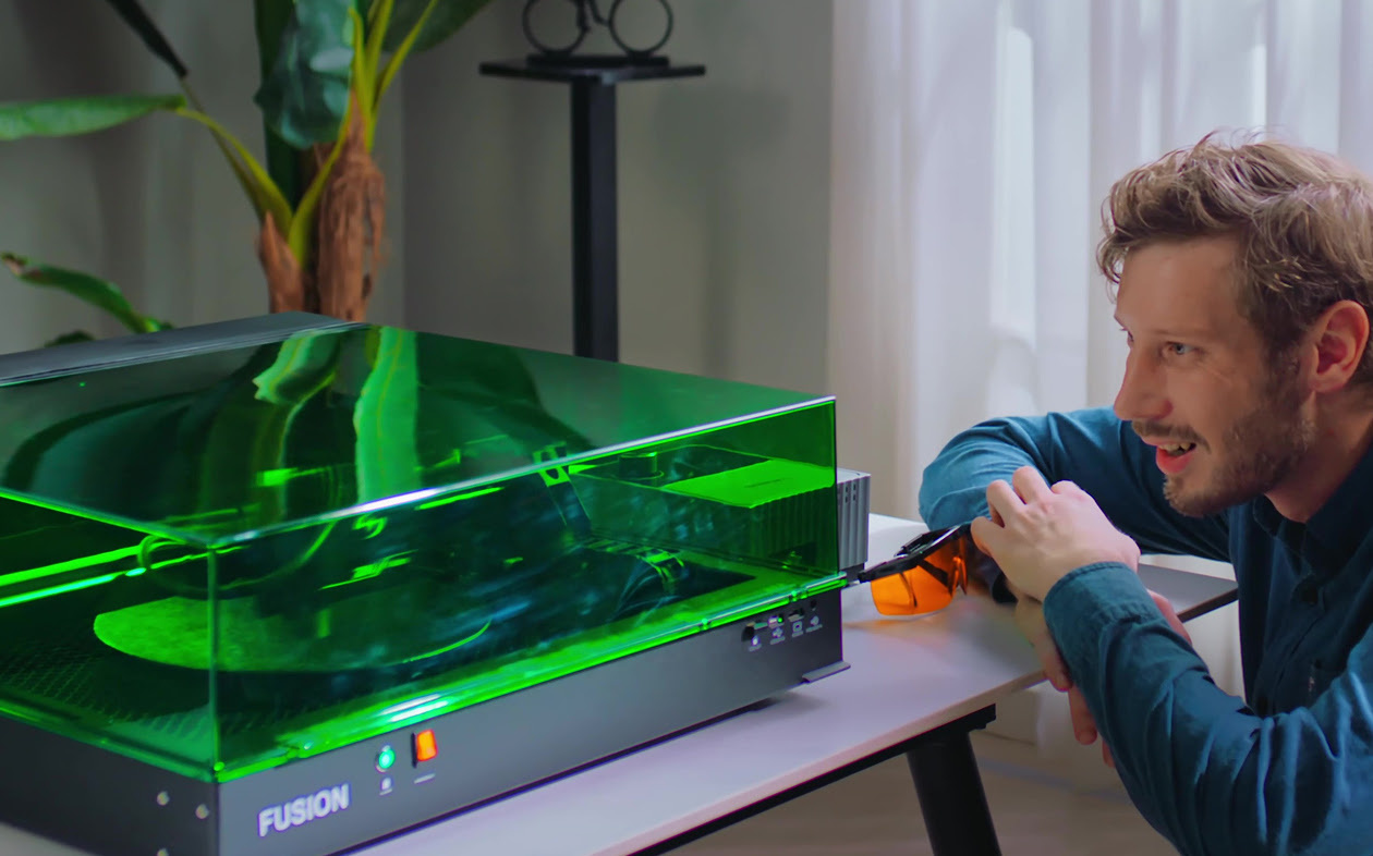 User safely operating the AtomStack Fusion desktop laser engraver inside its Class 1 green laser safety enclosure without safety glasses.
