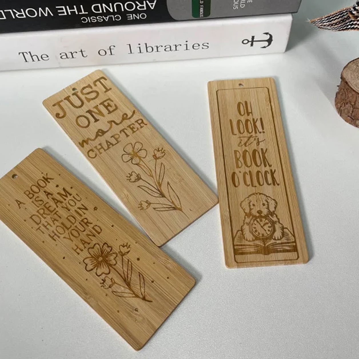 Three rectangular bamboo bookmarks featuring engraved reading quotes, floral designs, and a dog illustration, set near a stack of books.