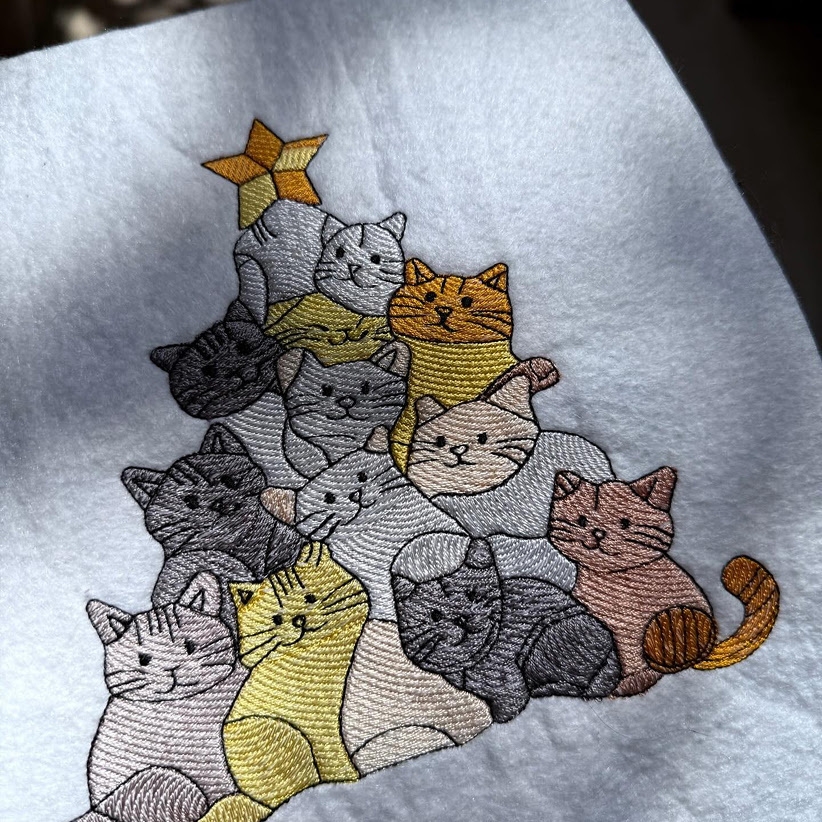 Toalla blanca con un diseño bordado de un montón de gatos y una estrella en la parte superior, como si fuera un árbol de Navidad.